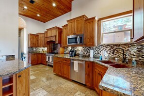 A kitchen with wooden cabinets, granite countertops, a stainless steel microwave, and a tiled backsplash. - Exquisite home with mountain views, fireplaces, game room & private Hot tub (Flagstaff)