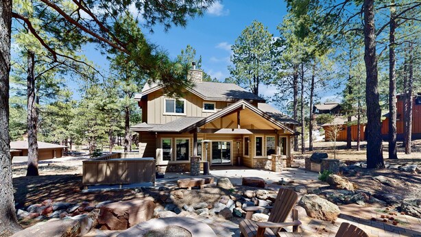 A lodge with a stone fireplace, wooden deck, and surrounding trees. - Exquisite home with mountain views, fireplaces, game room & private Hot tub (Flagstaff)