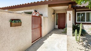 Une maison avec une entrée fermée par un portail, un panneau d’accueil et un cactus dans le jardin.