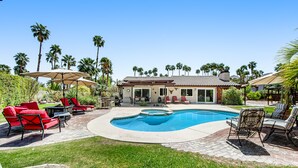 Un jardin avec une piscine, des chaises longues rouges et des palmiers.