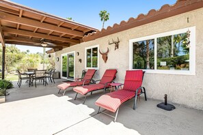Une terrasse extérieure dotée d’un espace couvert, d’une table à manger avec des chaises, et de fauteuils avec des coussins à rayures.