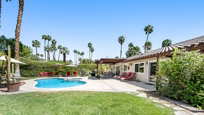 Un jardin avec une piscine, des chaises longues rouges et des palmiers.