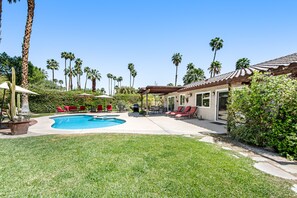 Un patio trasero con piscina, sillas reclinables rojas y palmeras.