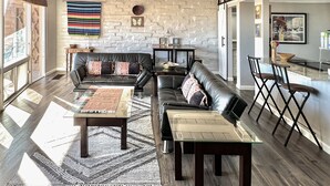Een ruime woonkamer met een stenen muur, leren banken, een eethoek met een marmeren tafel en een keuken op de achtergrond.