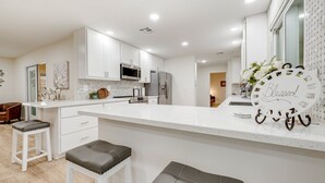 A modern kitchen with white cabinetry, stainless steel appliances, and a central island with stools. - Ground-Floor Home w/Valley Views, Central A/C, Fast WiFi, & Private Washer/Dryer (Sun City)