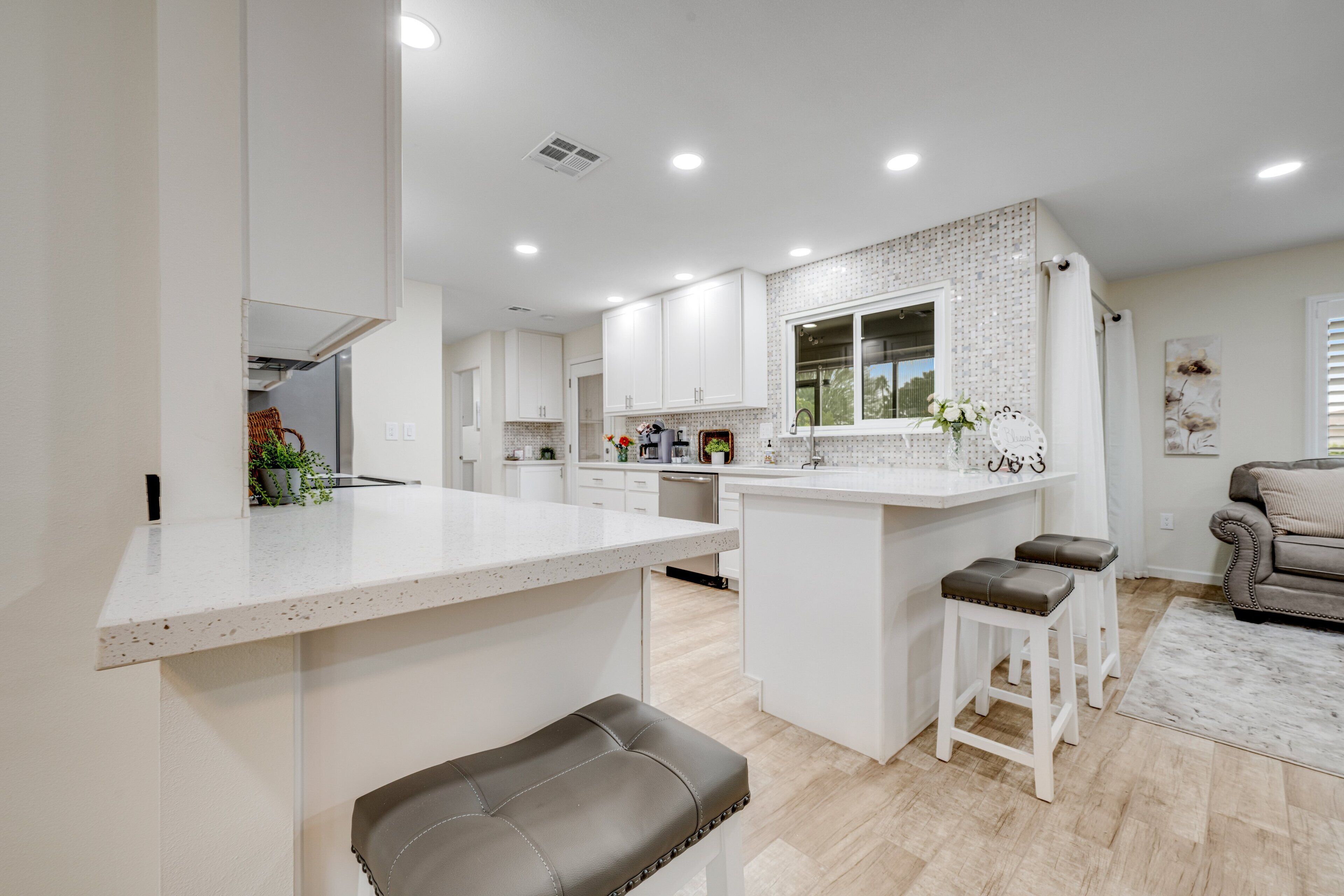 A modern kitchen with white cabinetry, a central island with bar stools, and a dining area with a sofa and a coffee table.