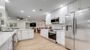 A modern kitchen with white cabinets, stainless steel appliances, and a wooden dining area. - Ground-Floor Home w/Valley Views, Central A/C, Fast WiFi, & Private Washer/Dryer (Sun City)