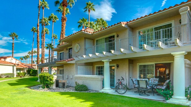A two-story house with a covered patio, palm trees, and a bicycle parked outside. - Eclectic dog-friendly condo with gated entrance, pool & grill (Palm Springs)