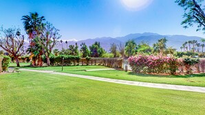 A well-maintained garden with a pathway, palm trees, and flowering bushes. - Eclectic dog-friendly condo with gated entrance, pool & grill (Palm Springs)