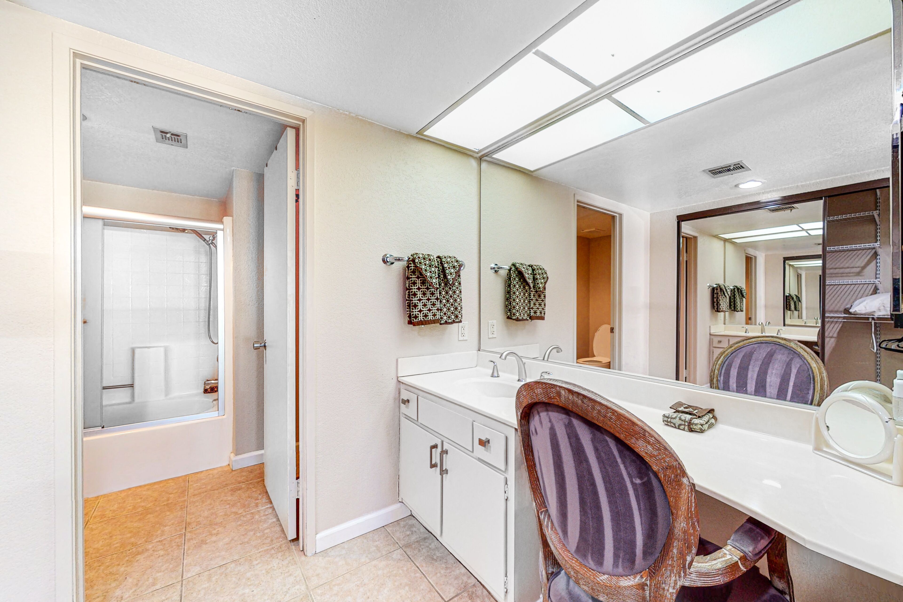 A bathroom with a bathtub, a sink, a mirror, and a vanity with a chair.