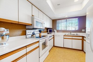 Una cocina moderna con armarios blancos, microondas integrado, hervidor y un lavabo.