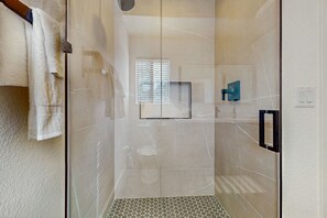 Eine moderne Dusche mit Glastüren, Fliesenboden und einem Fenster mit Jalousien.
