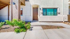 A modern house with a concrete driveway, a wooden pergola, and a small garden with green shrubs. - Beautiful dog-friendly condo with pool, central AC, & washer/dryer (Tucson)