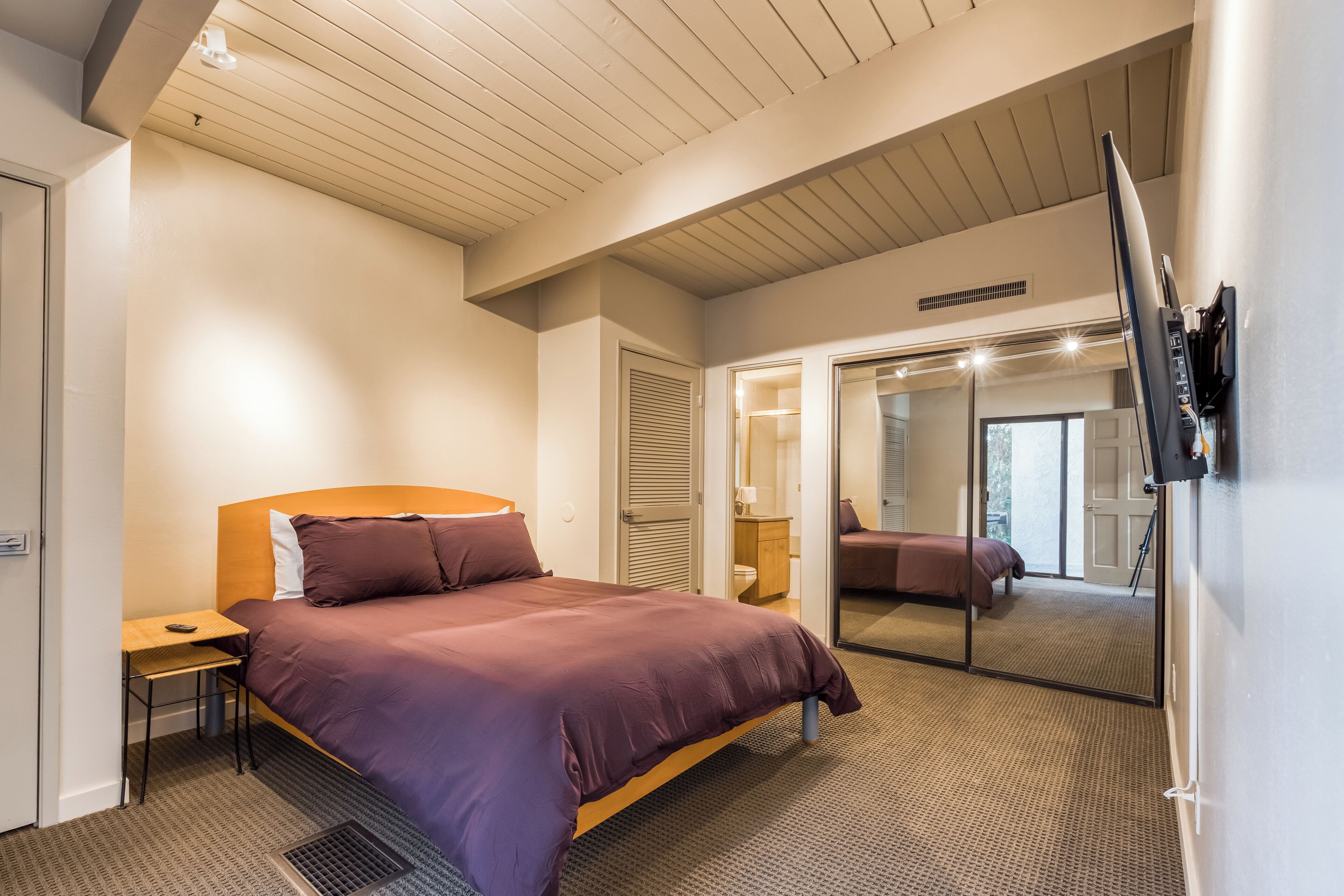 Une chambre d’hôtel moderne, dotée d’un grand lit, d’un bureau, d’un miroir et d’un téléviseur fixé au mur.