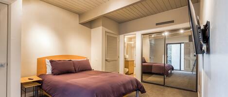 Une chambre d’hôtel moderne, dotée d’un grand lit, d’un bureau, d’un miroir et d’un téléviseur fixé au mur.