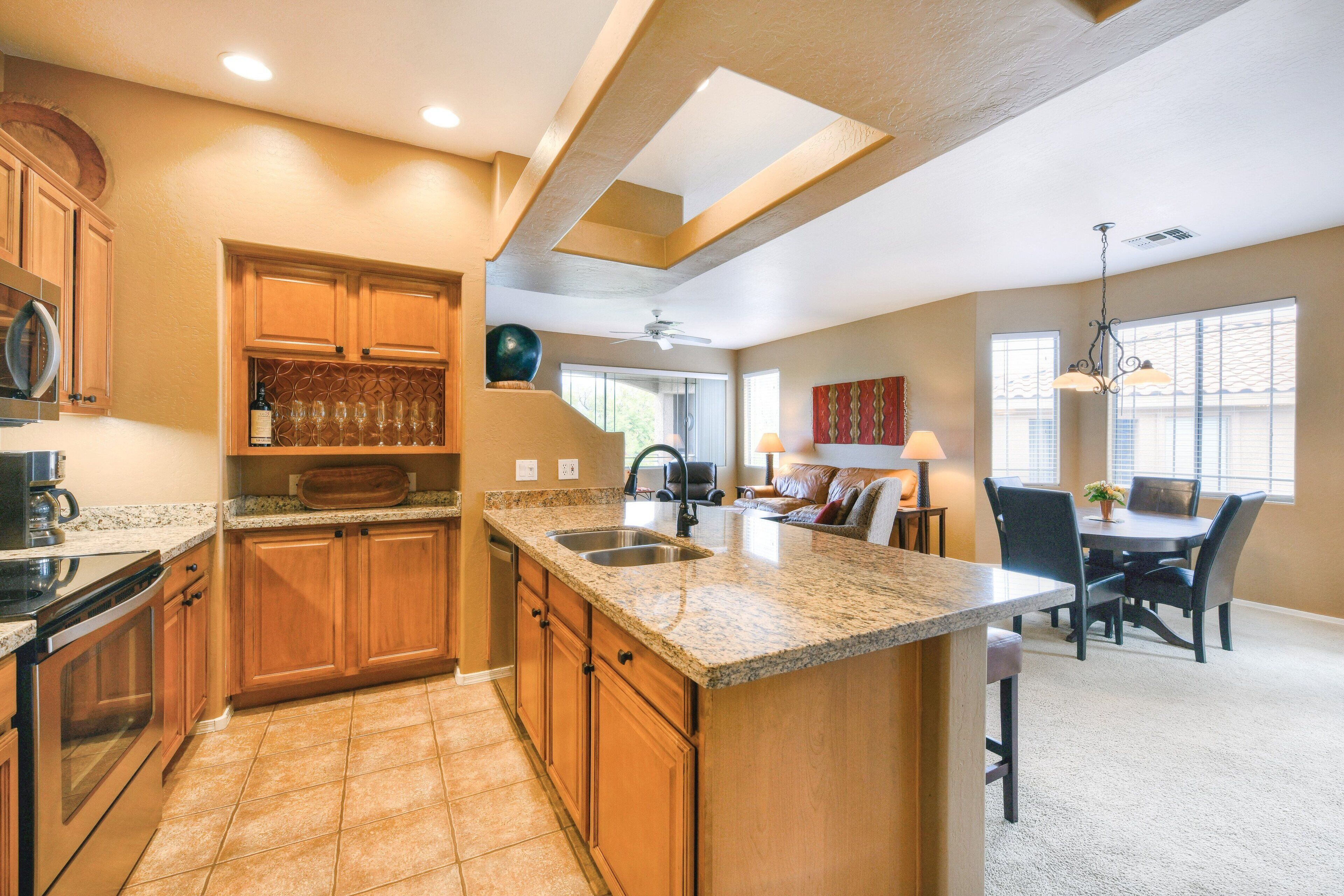 A kitchen with granite countertops, wooden cabinets, a built-in island, and a dining area with a table and chairs.