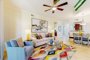 A living room with a sofa, coffee table, and a colorful rug. There is a dining area with a table and chairs. - Bright Dog Friendly condo with inviting patio, washer/dryer on a Golf Course (Cathedral City)