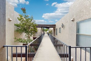 A narrow corridor with a metal railing, a tree, and a building with a garage door. - Charming Condo w/ Red Rock views, shared pool/hot tub & pickleball/tennis courts (Sedona)