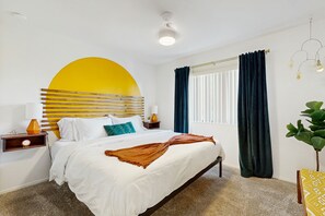 Una camera d'albergo con un letto, un comodino, una lampada, una finestra con tende e una pianta.
