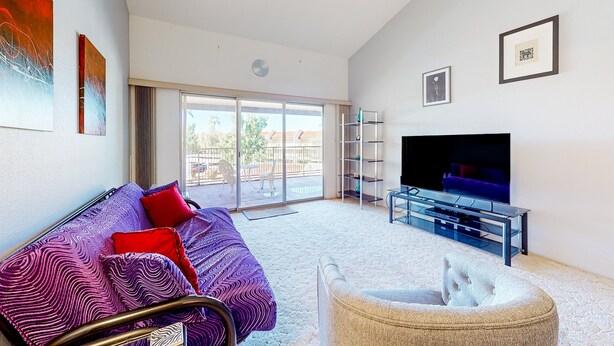 A modern living room with a sofa, a chair, a TV, and a balcony with glass doors. - Gorgeous condo with hot tub, pool, tennis court, & grilling area - lake access (Phoenix)