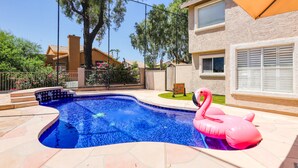 A swimming pool with a pink flamingo float, surrounded by a stone patio and a fence. - Delightful golf escape with pool, lawn games, pool table, fast WiFi & central AC (Phoenix)
