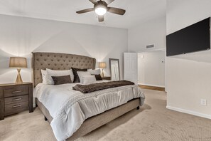 A bedroom with a tufted headboard, a large bed with white bedding, two bedside tables with lamps, a ceiling fan, a flat-screen TV mounted on the wall, and a wardrobe. - Contemporary home with a private pool, hot tub & fast WiFi (Scottsdale)