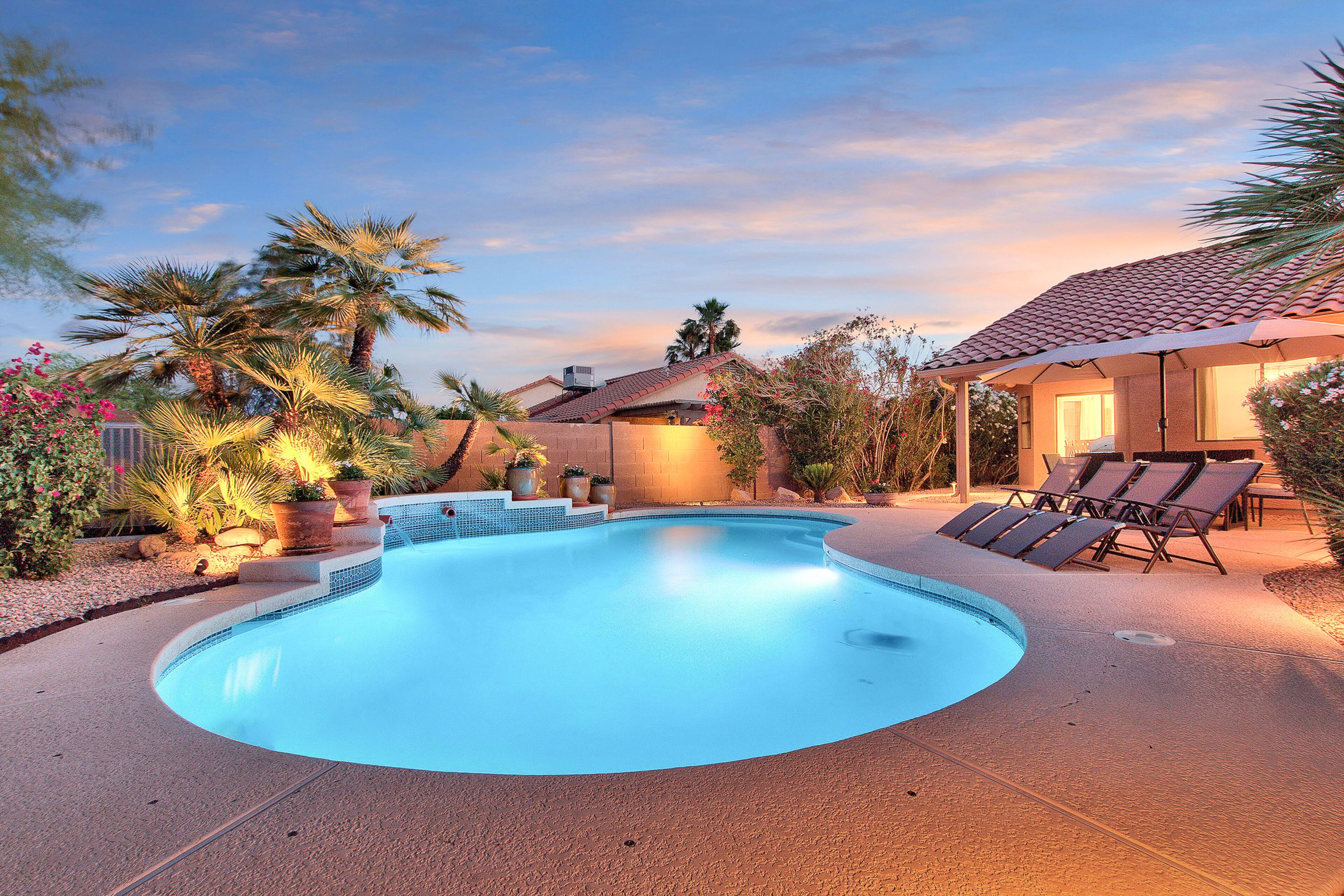 A swimming pool with a curved edge, surrounded by a patio area with lounge chairs and potted plants.