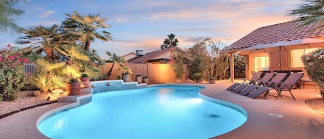 A swimming pool with a curved edge, surrounded by a patio area with lounge chairs and potted plants.