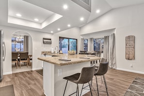 A modern kitchen with a central island, bar stools, and a dining area with a view. - Contemporary home with a private pool, hot tub & fast WiFi (Scottsdale)