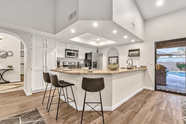 A modern kitchen with a central island, bar stools, and a view of the backyard. - Contemporary home with a private pool, hot tub & fast WiFi (Scottsdale)