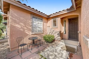 Una casa con patio que cuenta con dos sillas, una mesa, una puerta y una ventana.