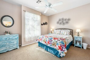 A bedroom with a bed, two bedside tables, a ceiling fan, a dresser, a mirror, and a window with curtains.