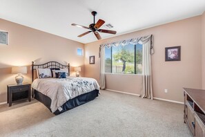 A bedroom with a bed, a nightstand, a ceiling fan, a window with curtains, and a dresser.
