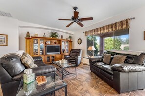 A living room with a leather sofa, a glass coffee table, a TV, and a cabinet with decorative items.