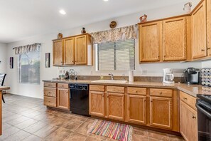 A kitchen with wooden cabinets, a dishwasher, a coffee maker, and a window with blinds.