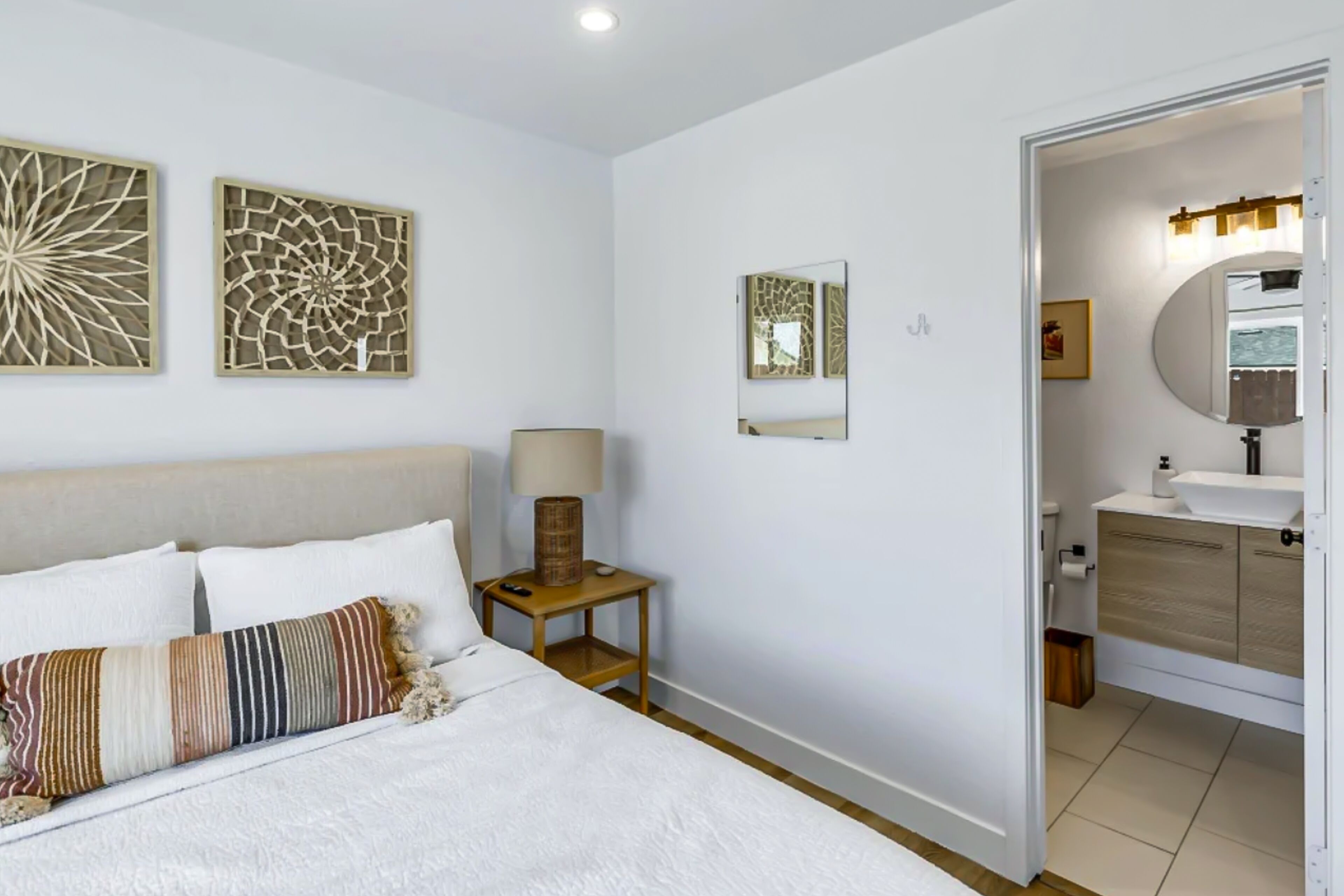 A hotel room with a bed, bedside table, lamp, and a bathroom visible through an open door.