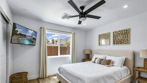 Quarto com cama, ventilador de teto, televisão e janela com cortinas.