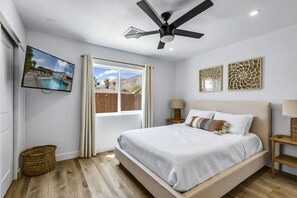 Ein Schlafzimmer mit einem Bett, einem Deckenventilator, einem Fernseher und einem Fenster mit Vorhängen.