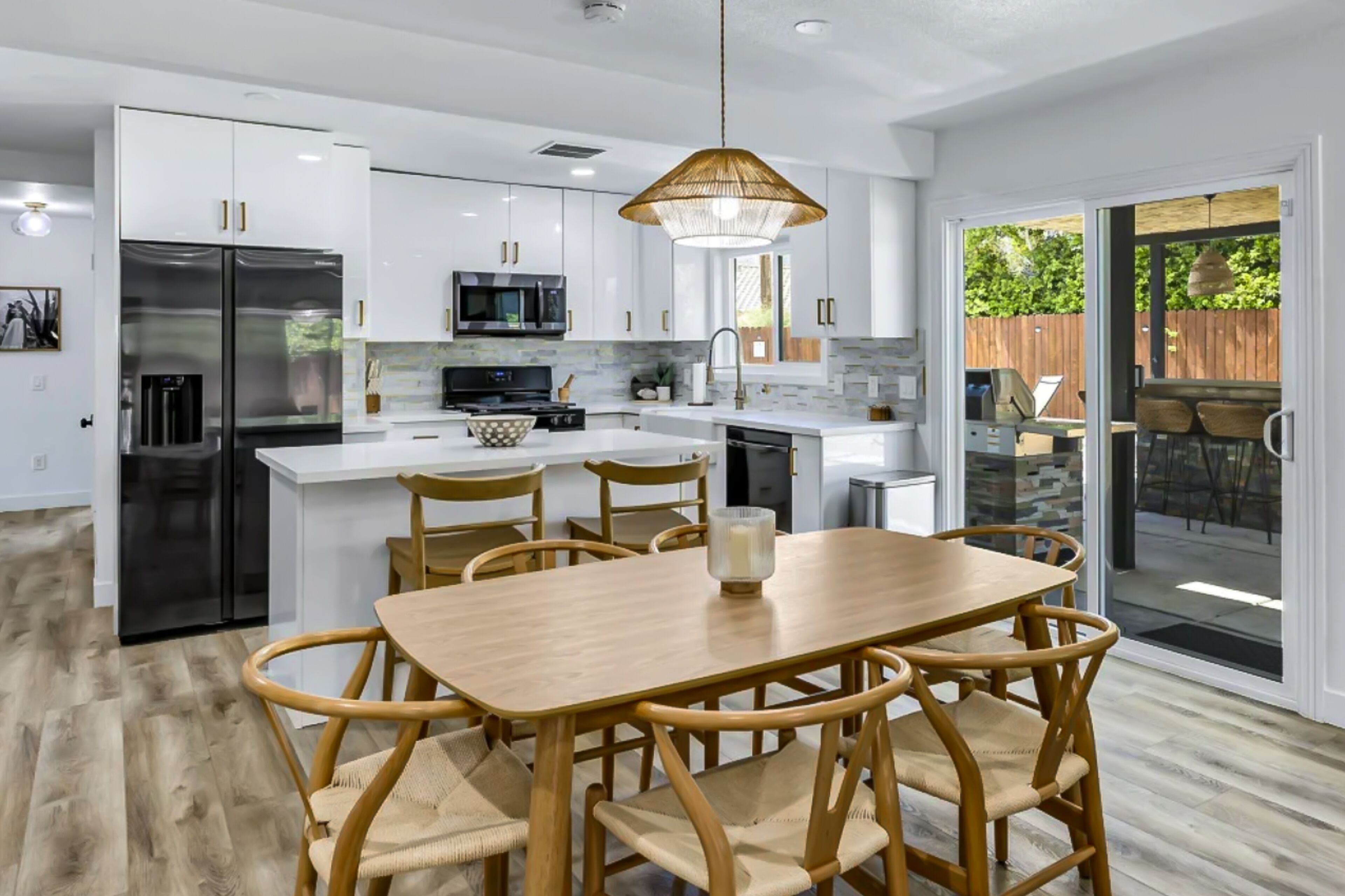 Une cuisine moderne avec des meubles blancs, un îlot central et un coin repas doté de chaises en bois.