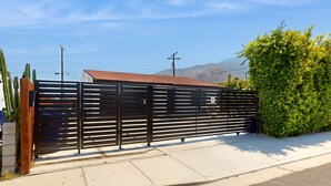 Uma área cercada com grade de metal, calçada de concreto e um arbusto verde.
