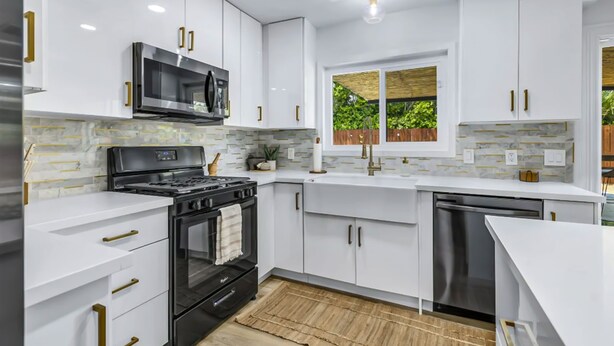Uma cozinha moderna com armários brancos, eletrodomésticos de aço inoxidável e uma janela com vista para o verde.