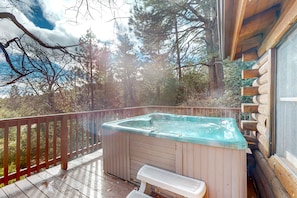 Un jacuzzi en una terraza de madera con vistas a árboles y un cielo nublado.