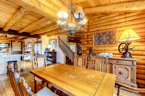 Un interior de madera con una mesa de comedor, sillas, una araña y una escalera que sube a otro nivel.