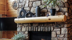 Ein Kamin aus Stein mit einem Fernseher darüber, eine Holzbalkendecke und ein Sofa im Vordergrund.