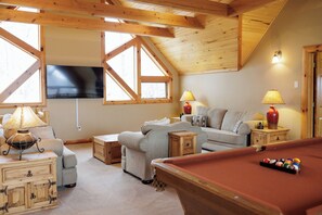 A cozy living room with a pool table, a sofa, and a television.
