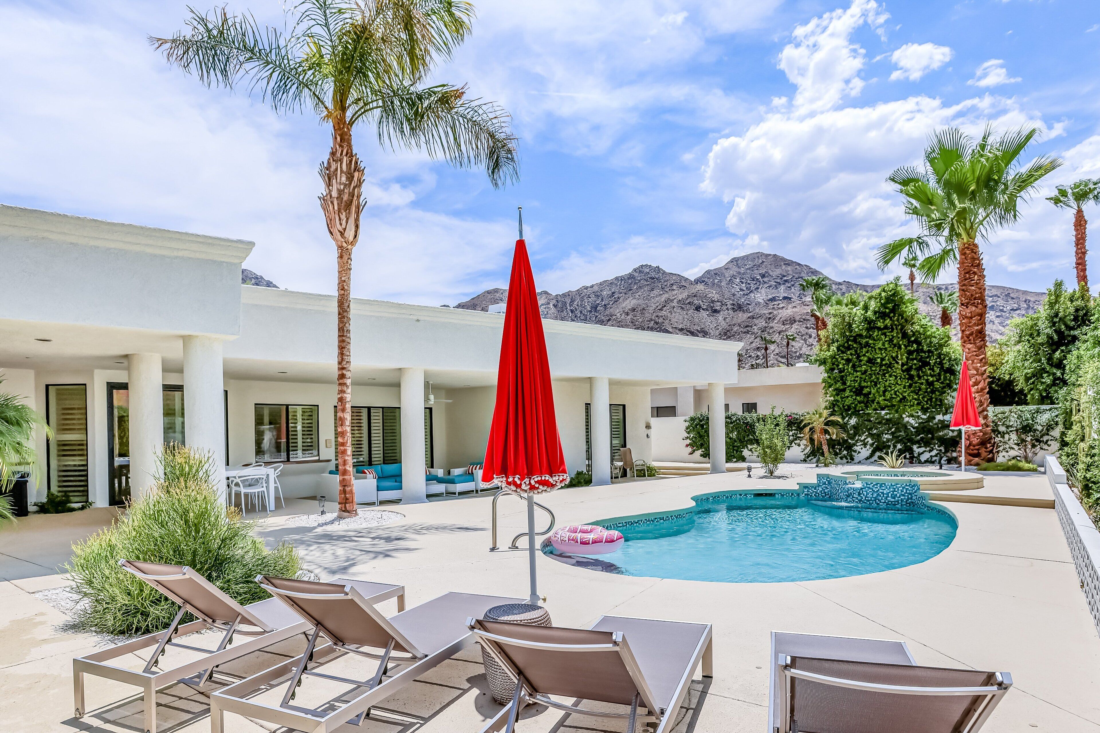 A pool area with lounge chairs, a red umbrella, and palm trees.