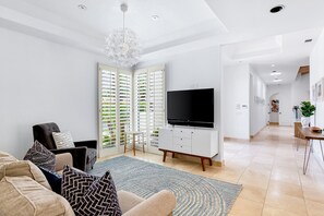 A modern living room with a sofa, TV, and a dining area with a table and chairs. - Gorgeous home with private pool, high-speed WiFi, central AC, & EV charger (Indian Wells)