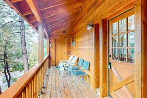 A wooden cabin with a porch, wooden benches, and a door with glass panels. - Charming dog-friendly home with covered deck, W/D, & mountain view (Idyllwild)