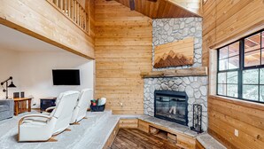 A wooden interior with a stone fireplace, seating area, and a television.