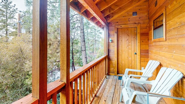 A wooden cabin with a porch, two Adirondack chairs, and a door.